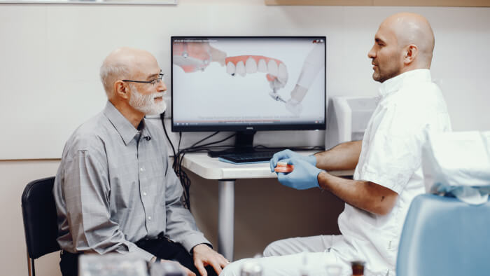 Vecchio seduto sul computer dell'ufficio del dentista con impianti dentali